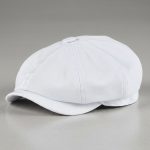 Casquette gavroche blanche posée sur béton gris, photo studio produit fond neutre
