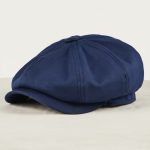 Casquette gavroche bleu marine posée sur lin blanc cassé, photo studio produit