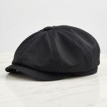 Casquette gavroche noire posée sur marbre blanc, photo studio produit fond clair